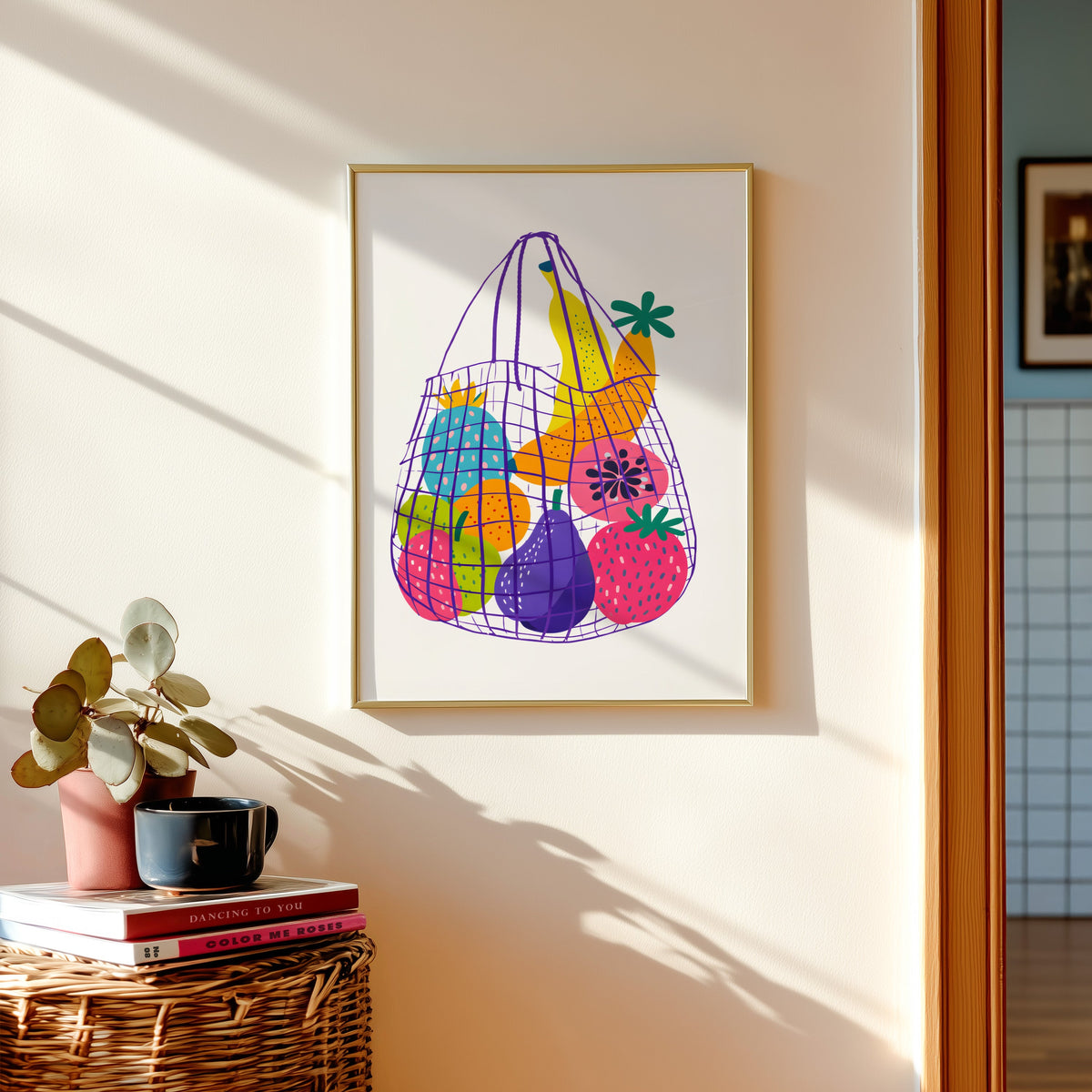 Fruit market bag print in a gold frame above a basket of books and a pilea plant