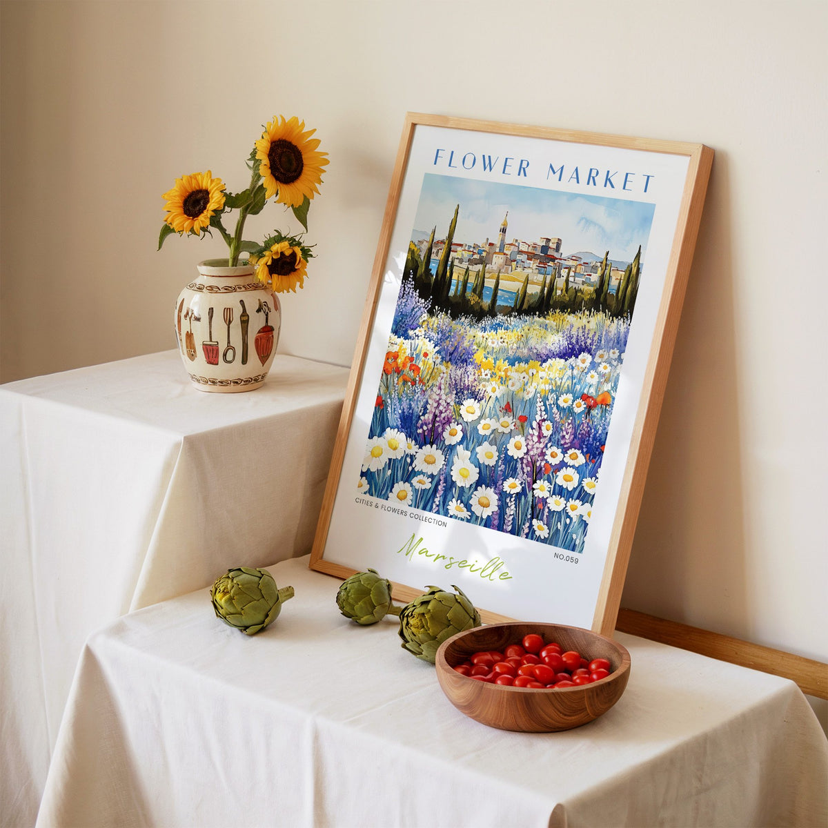 Marseille flower market print in an oak frame leaning on a linen-draped table beside a vase of sunflowers