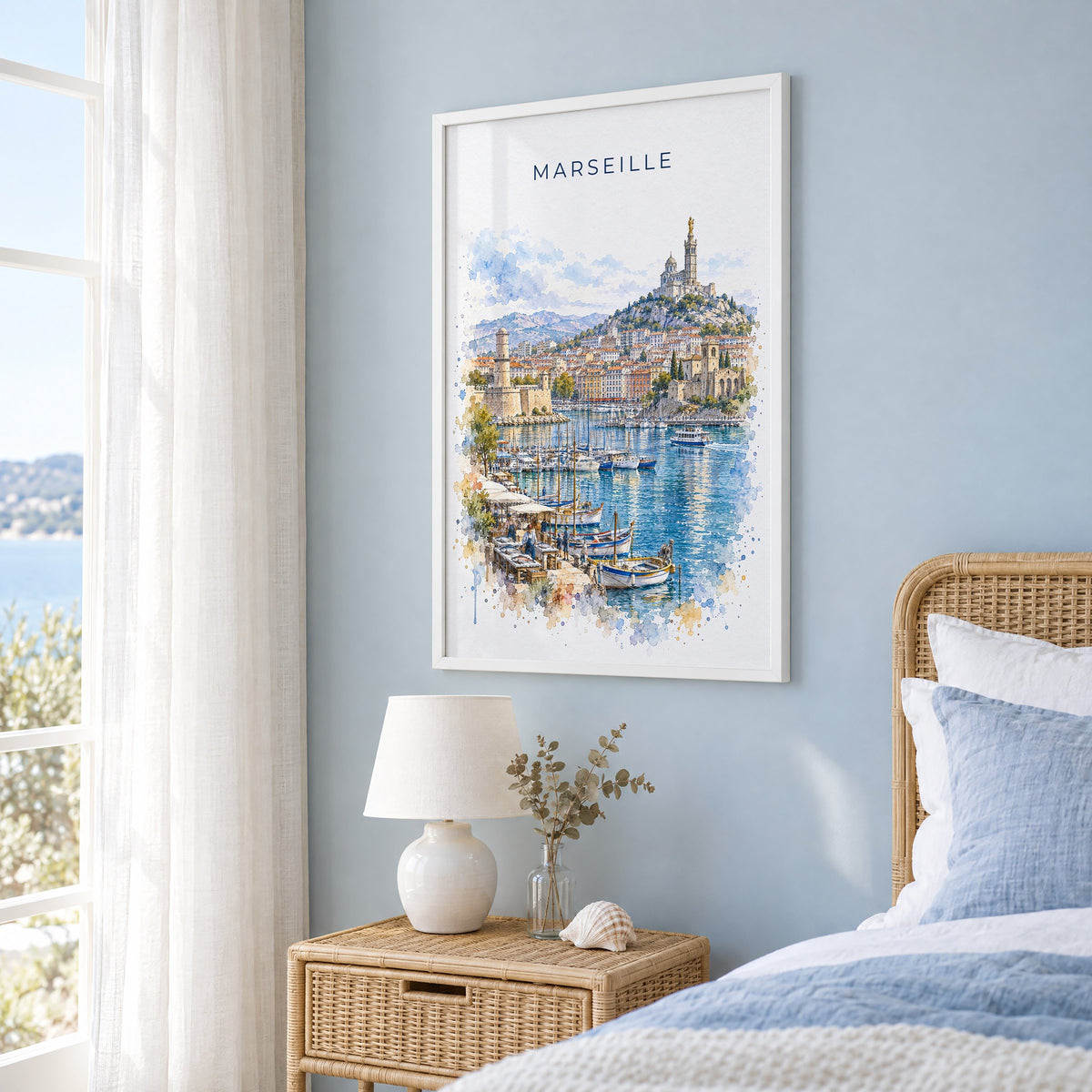 Marseille watercolor print in a white frame on a pale blue wall beside a rattan bed in a coastal bedroom