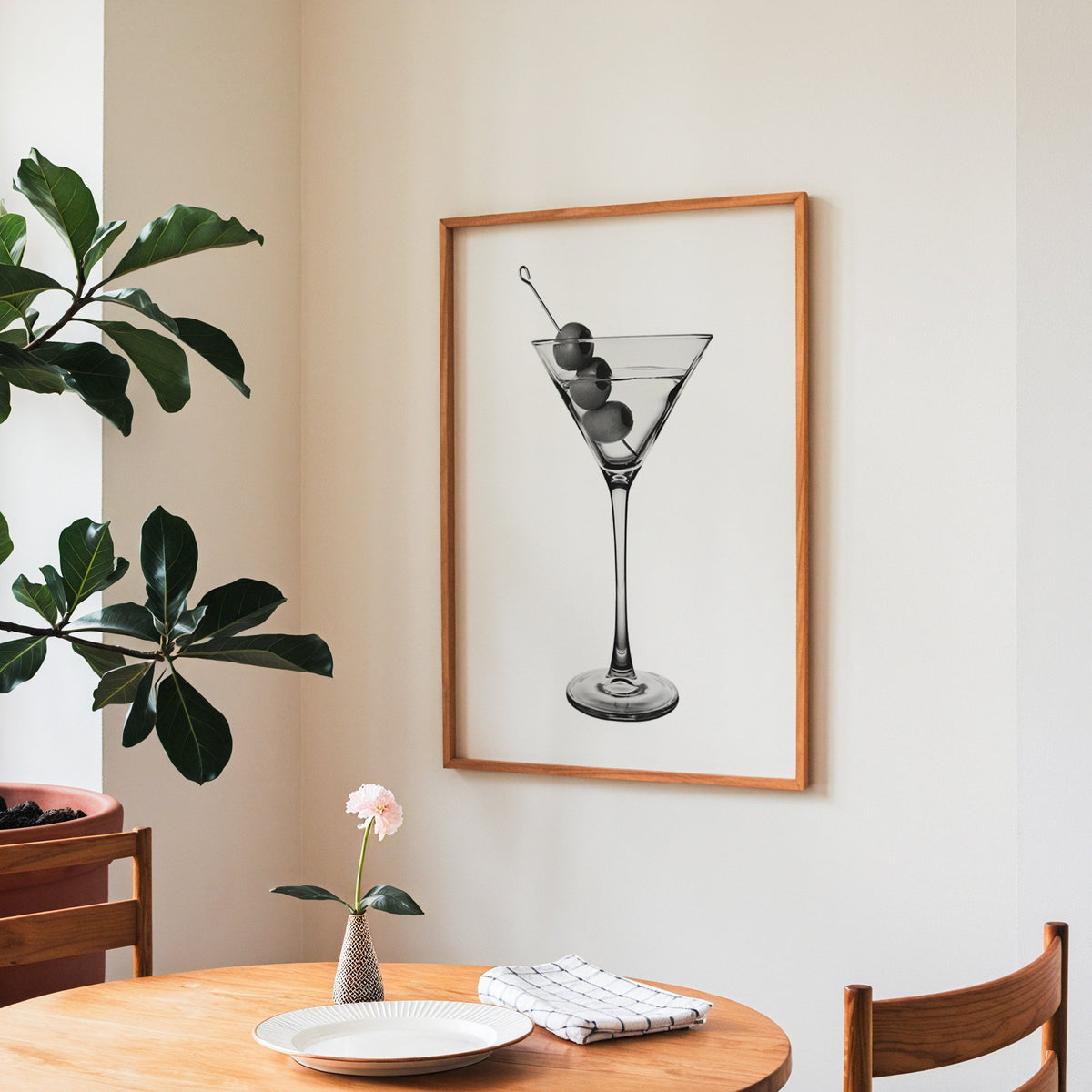 Martini glass with three olives on white print in a teak frame above a round wooden dining table