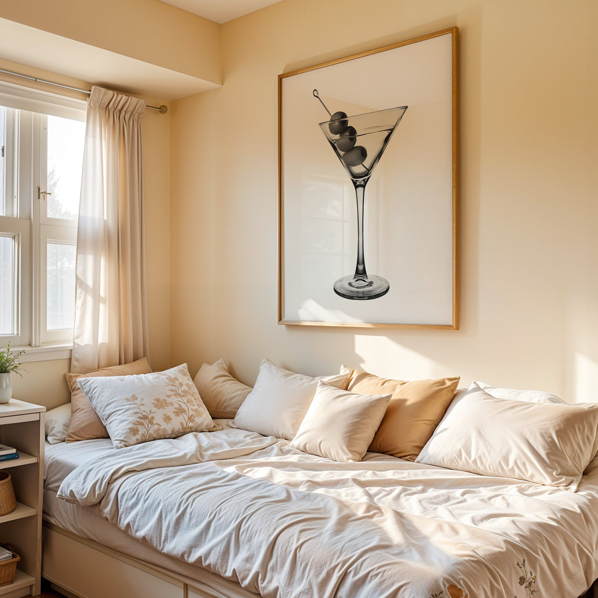 Martini glass with three olives on white print in an oak frame above a cream daybed in a sunny bedroom