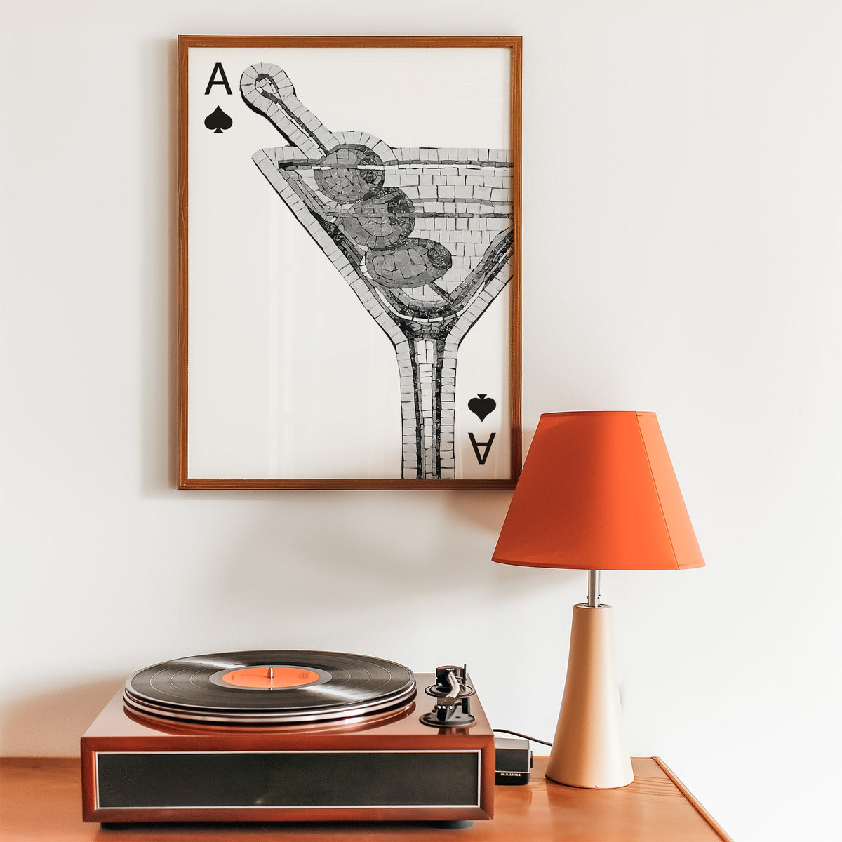 Mosaic martini glass on an ace of spades card print in a walnut frame above a record player and orange lamp