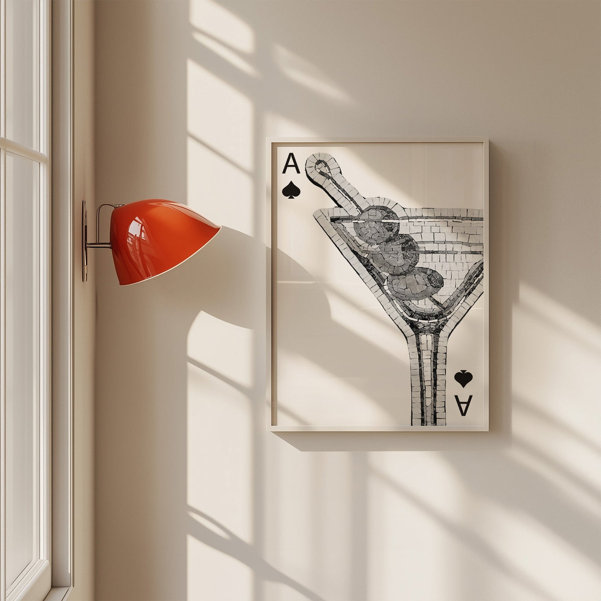 Mosaic martini glass on an ace of spades card print in a white frame on a sunlit wall beside a red sconce
