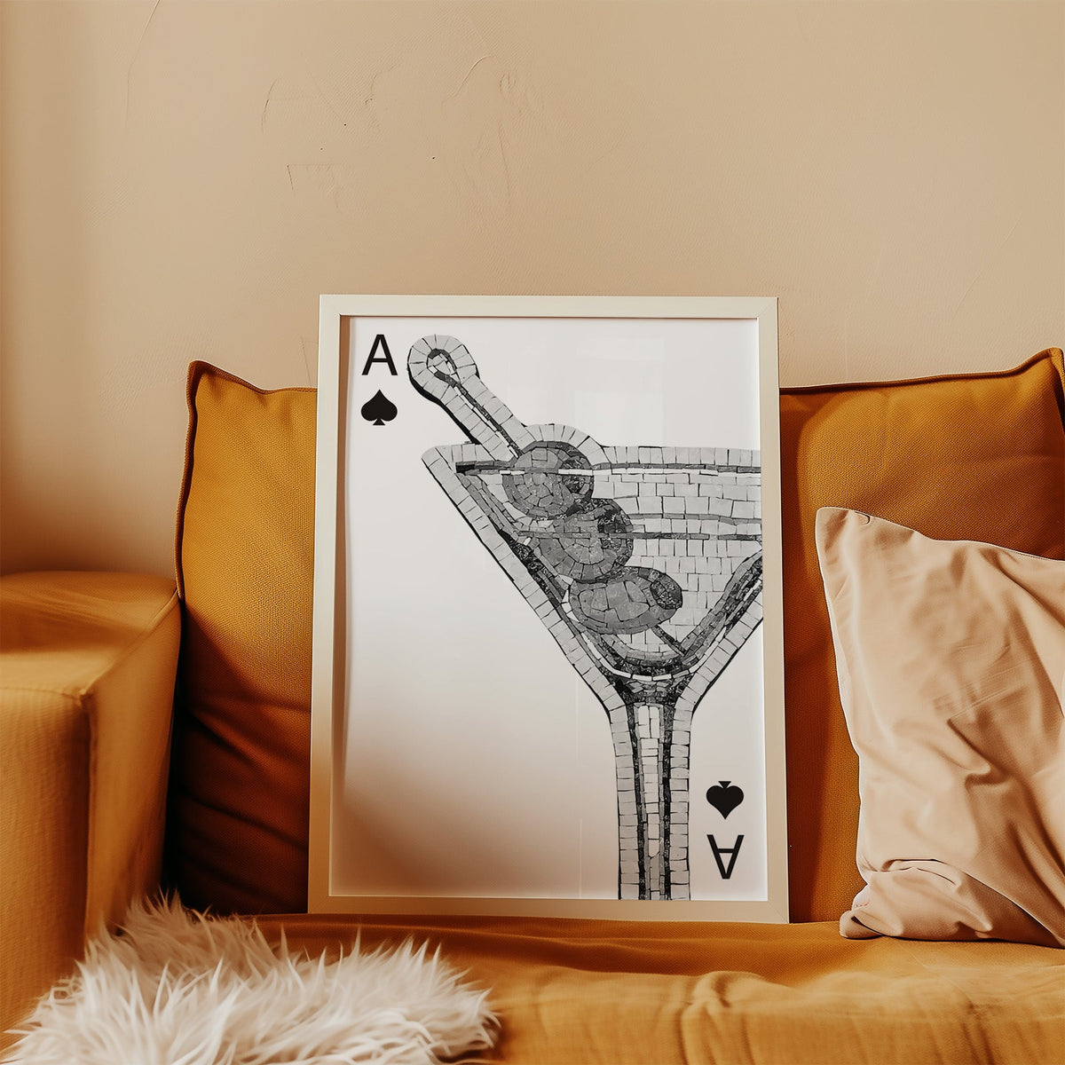 Mosaic martini glass on an ace of spades card print in a white frame leaning on a mustard velvet sofa