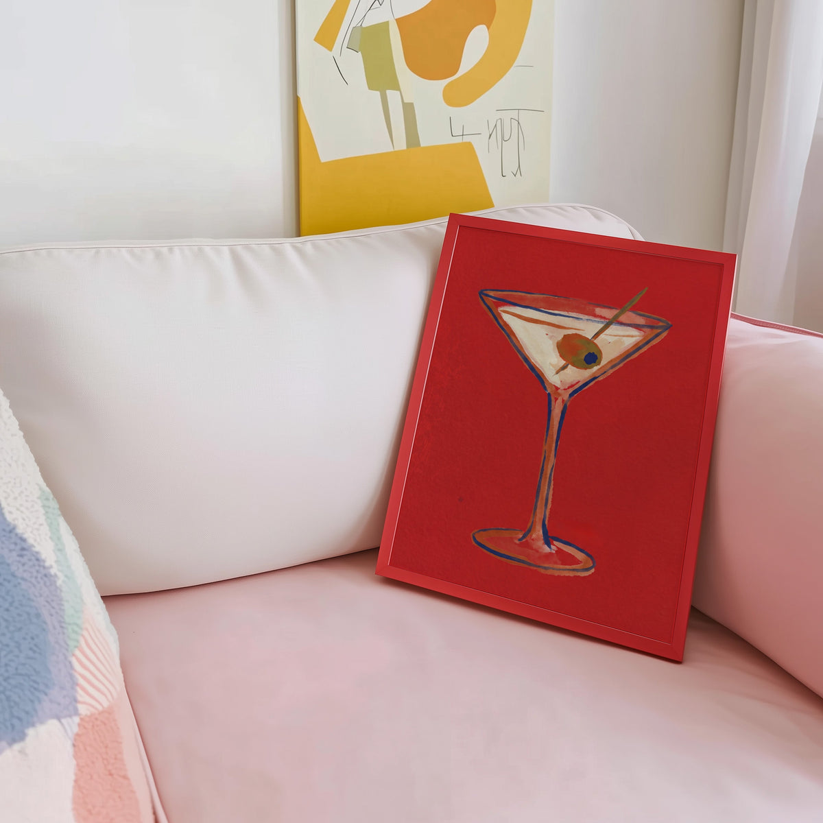 Olive martini print shown in a red frame leaning on a blush pink sofa