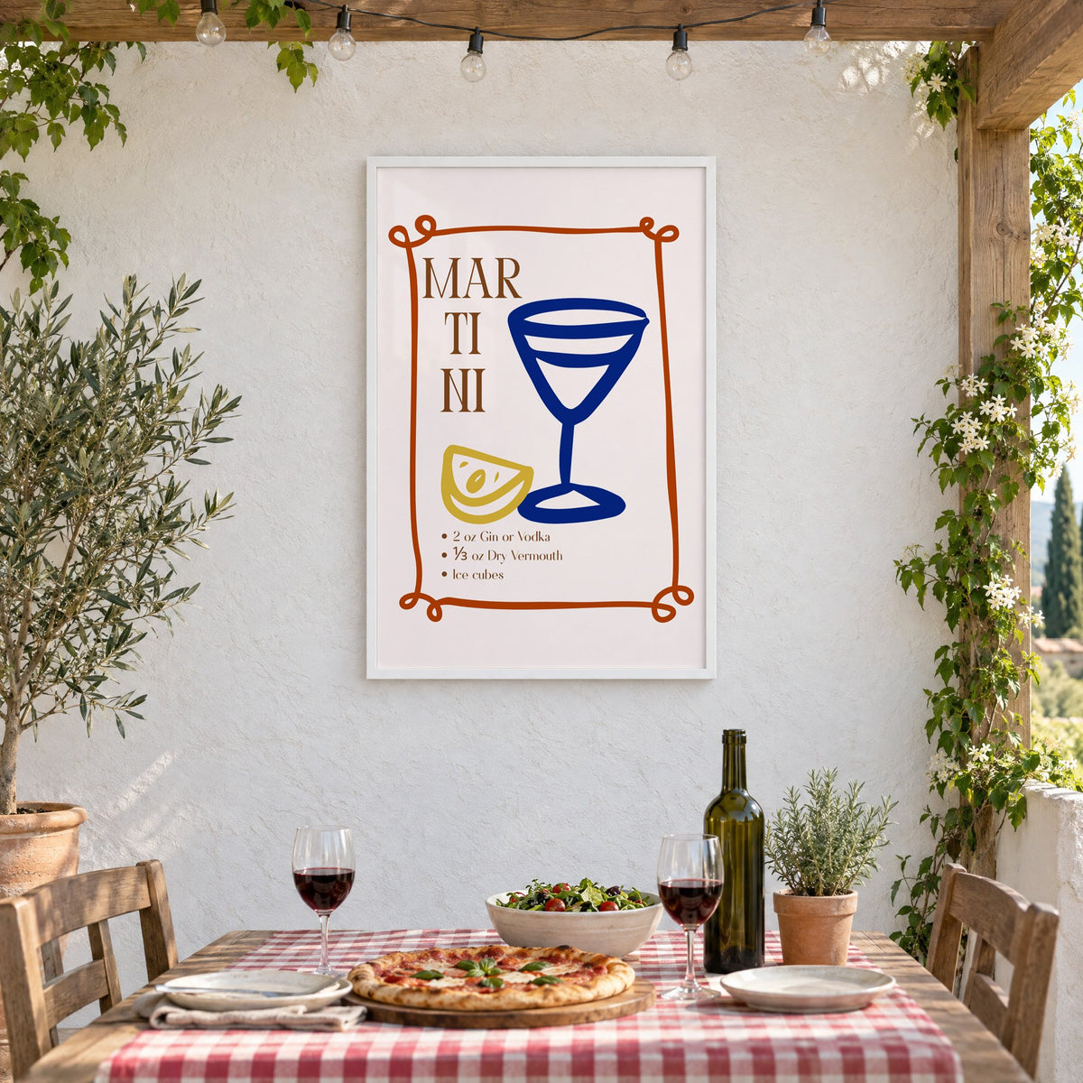 MARTINI recipe navy glass lemon print in a white frame on a stucco wall above a checked-cloth table with pizza and red wine