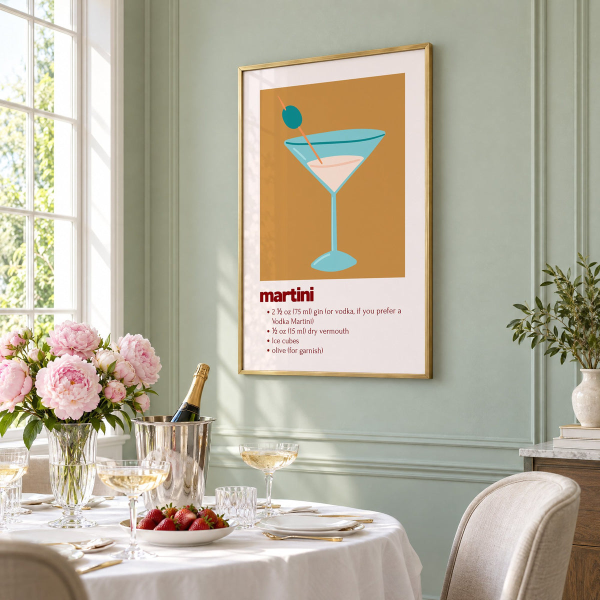 martini recipe olive glass ochre card print in a brass frame on a sage wall above a brunch table with champagne and peonies, seen at an angle