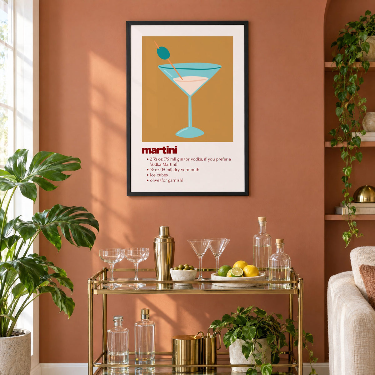 martini recipe olive glass ochre card print in a black frame on a terracotta wall above a brass bar cart with coupes and citrus