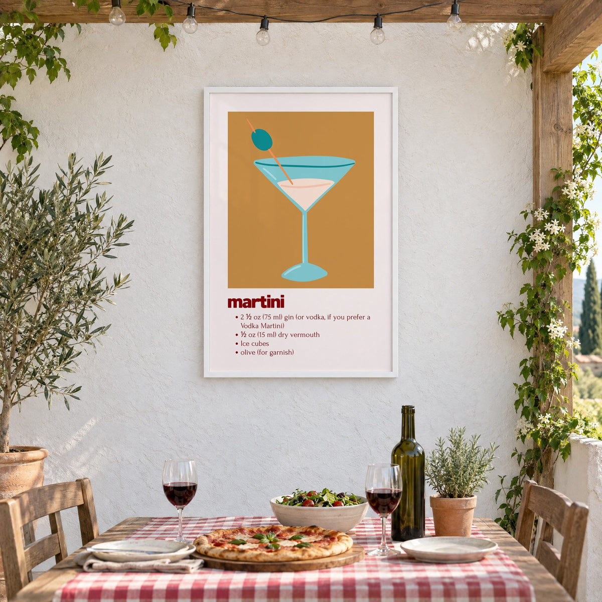 martini recipe olive glass ochre card print in a white frame on a stucco wall above a checked-cloth table with pizza and red wine