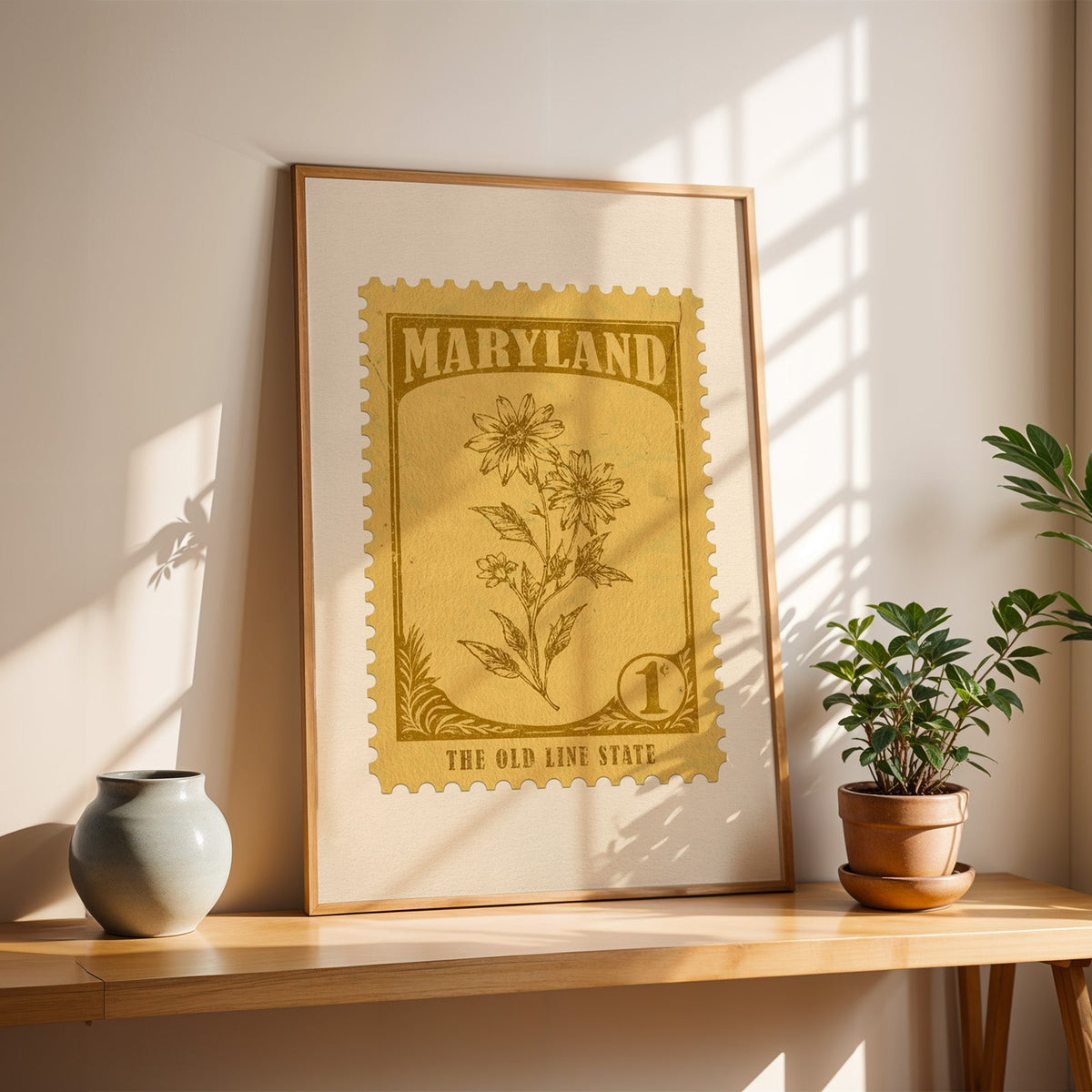 Maryland Black-Eyed Susan stamp print in a light oak frame leaning on a wooden table beside a stoneware vase
