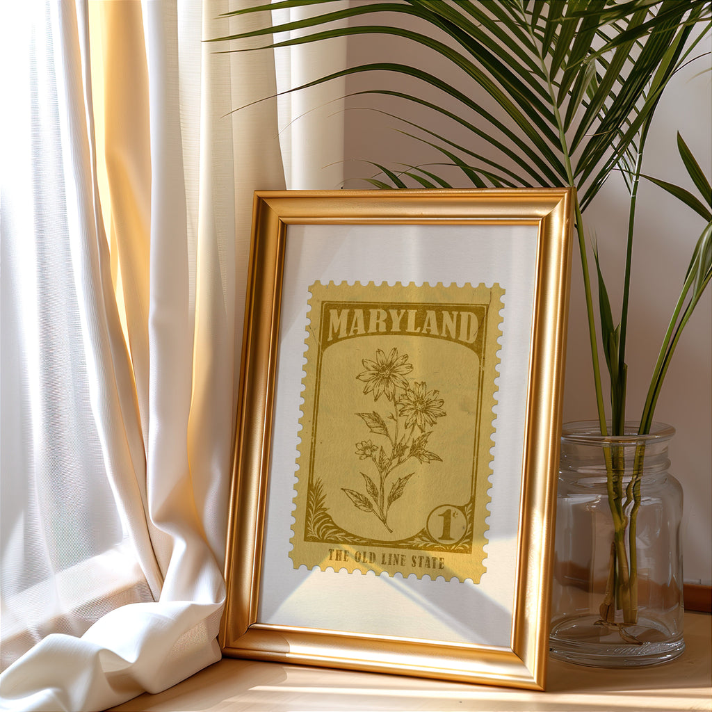 Maryland stamp print in a gold frame leaning by a cream curtain with a palm in a glass jar