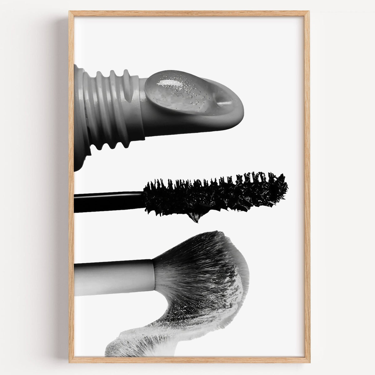 Macro gloss wand, mascara and blush brush print in a light oak frame on a plain white wall
