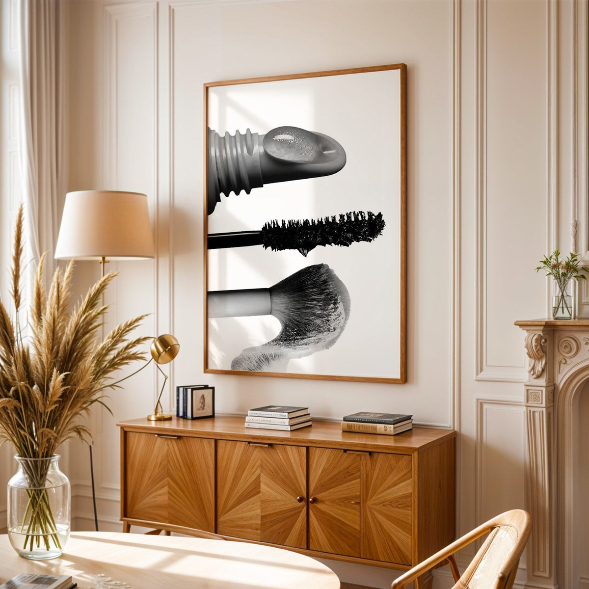 Macro gloss wand, mascara and blush brush print in an oak frame above a sunburst wood sideboard with pampas grass
