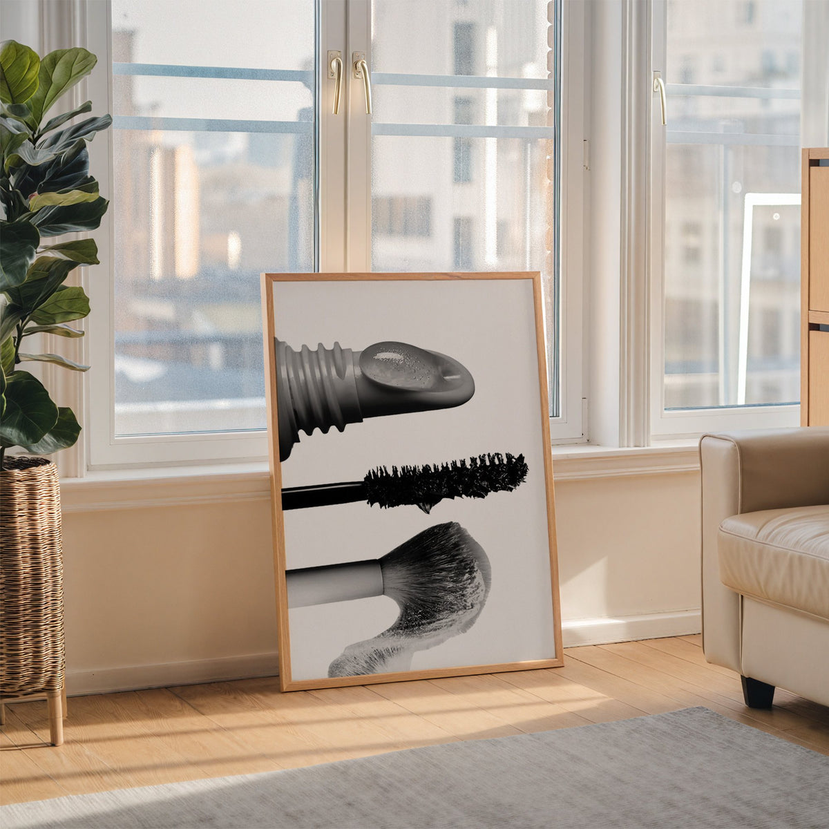 Macro gloss wand, mascara and blush brush print in an oak frame leaning on the floor beside a fiddle leaf fig