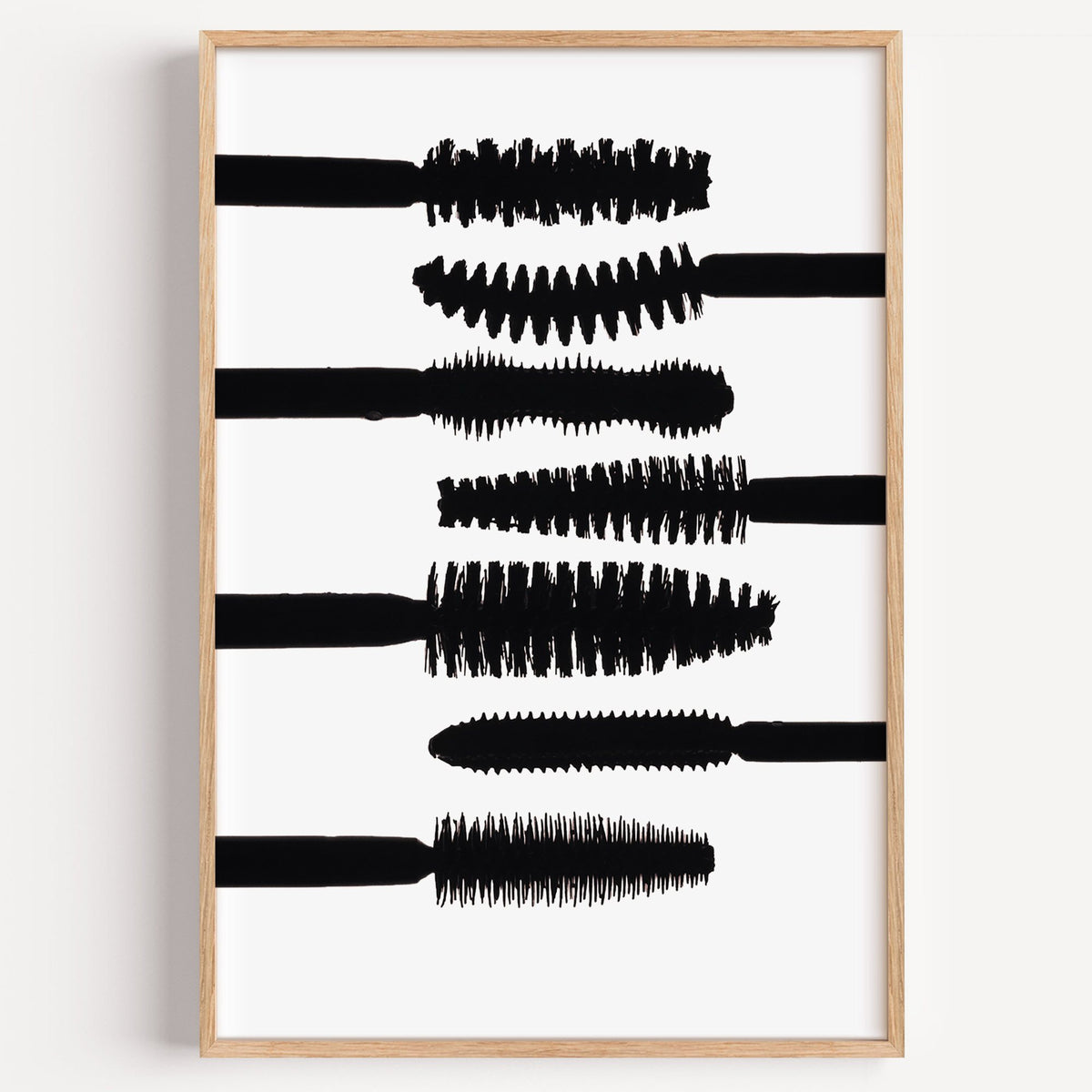 Seven mascara wand silhouettes on white print in a light oak frame on a plain white wall