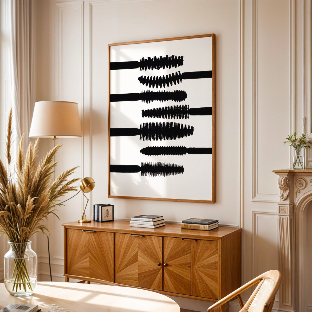 Seven mascara wand silhouettes on white print in an oak frame above a sunburst wood sideboard with pampas grass
