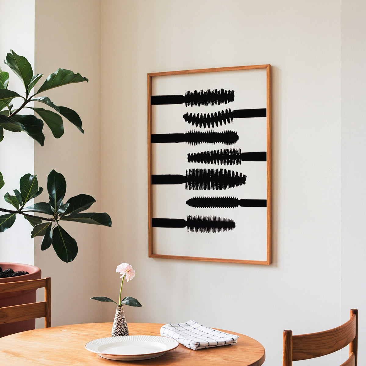 Seven mascara wand silhouettes on white print in a teak frame above a round wooden dining table