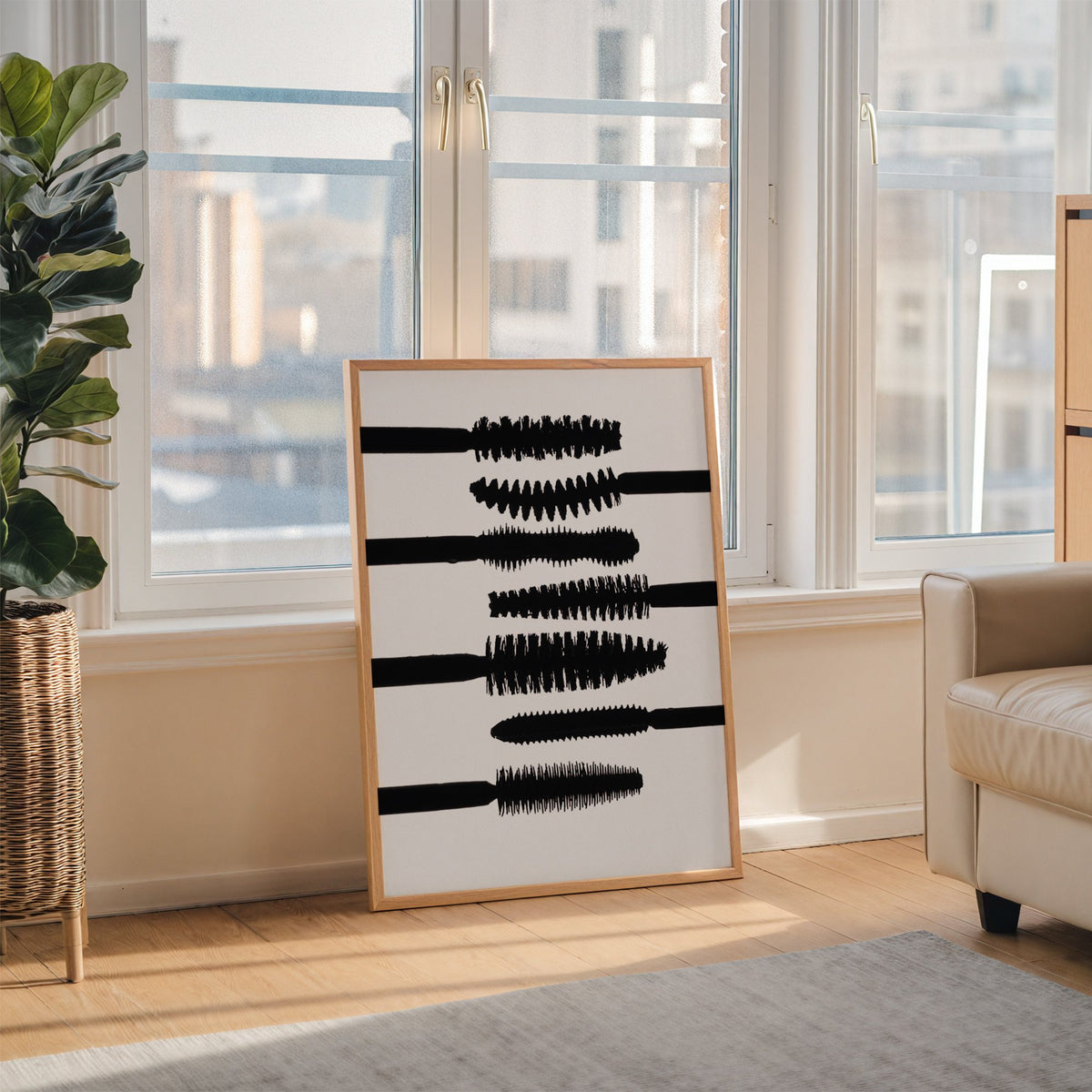 Seven mascara wand silhouettes on white print in an oak frame leaning on the floor beside a fiddle leaf fig