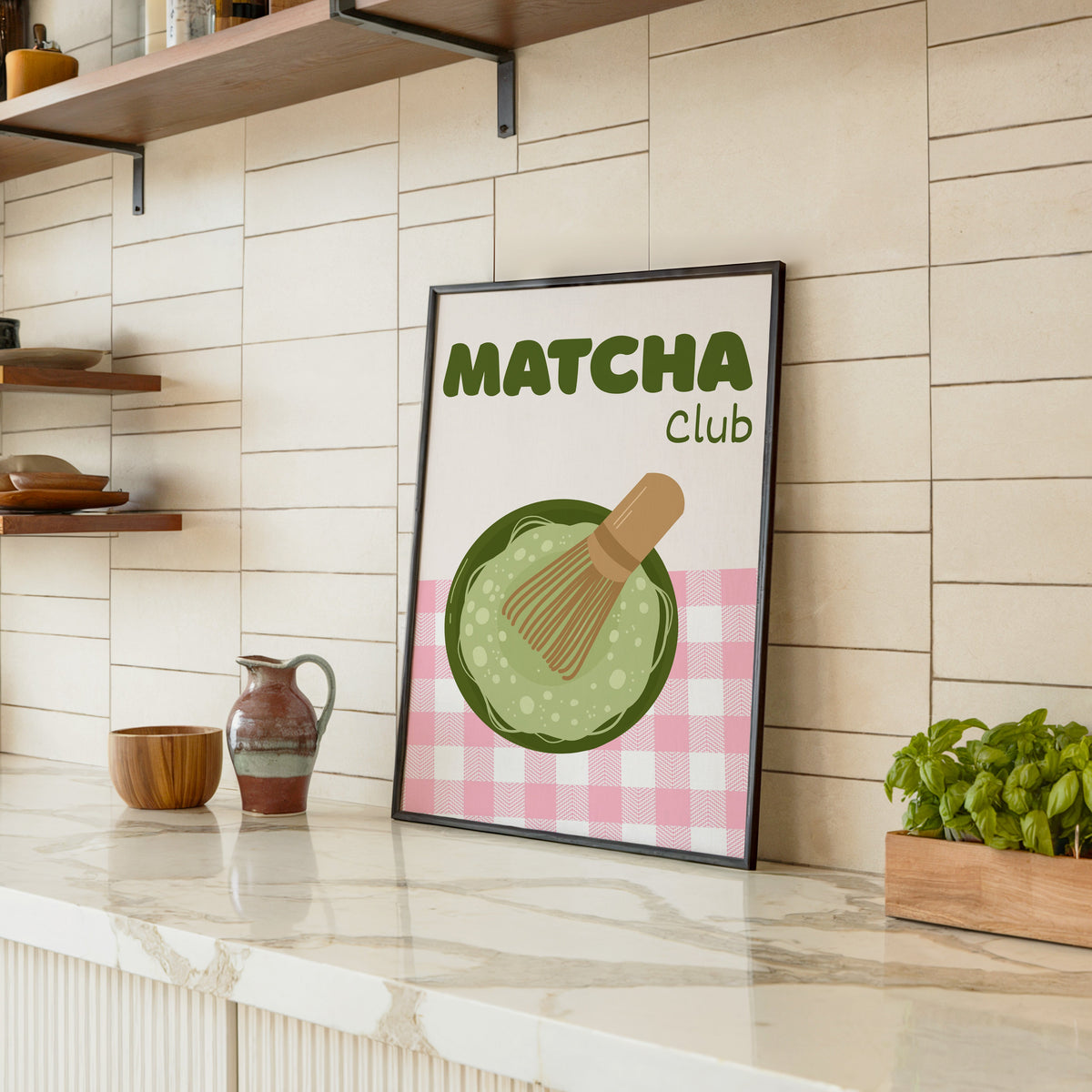 Matcha Club print in a black frame leaning on a marble counter in a tiled kitchen