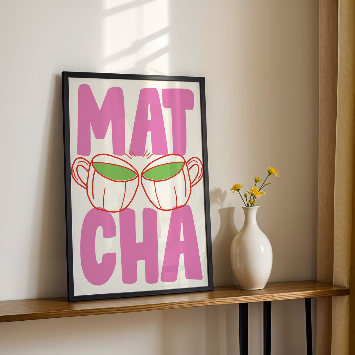 Matcha two cups print in a black frame on a console table with yellow daisies