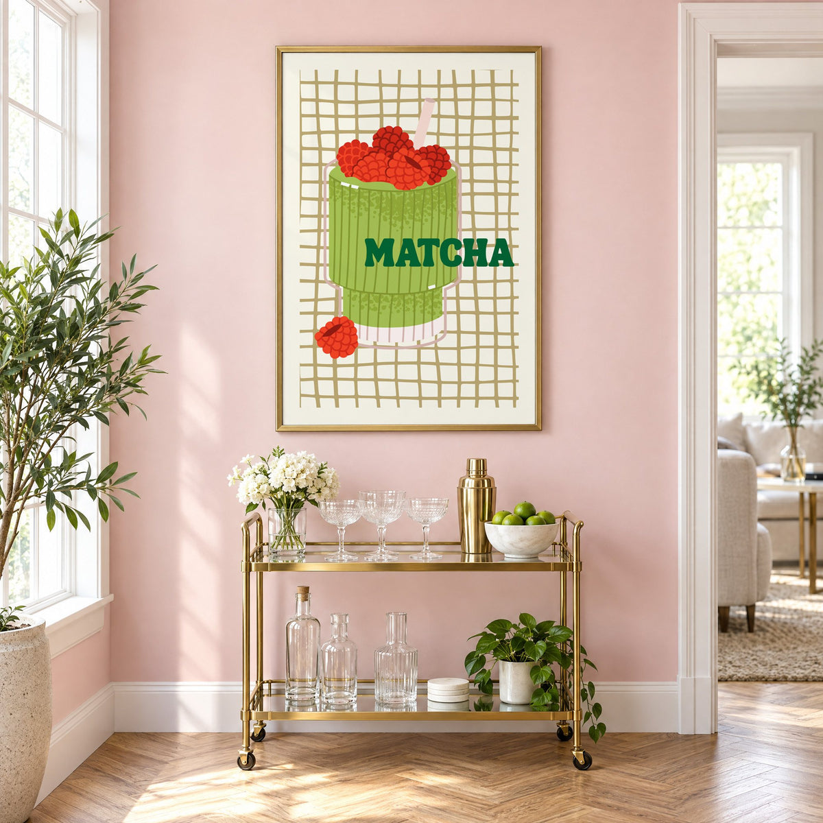 MATCHA raspberry glass on grid print in a brass frame on a blush pink wall above a gold bar cart with glassware