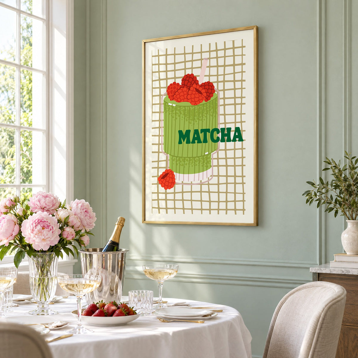 MATCHA raspberry glass on grid print in a brass frame on a sage wall above a brunch table with champagne and peonies, seen at an angle