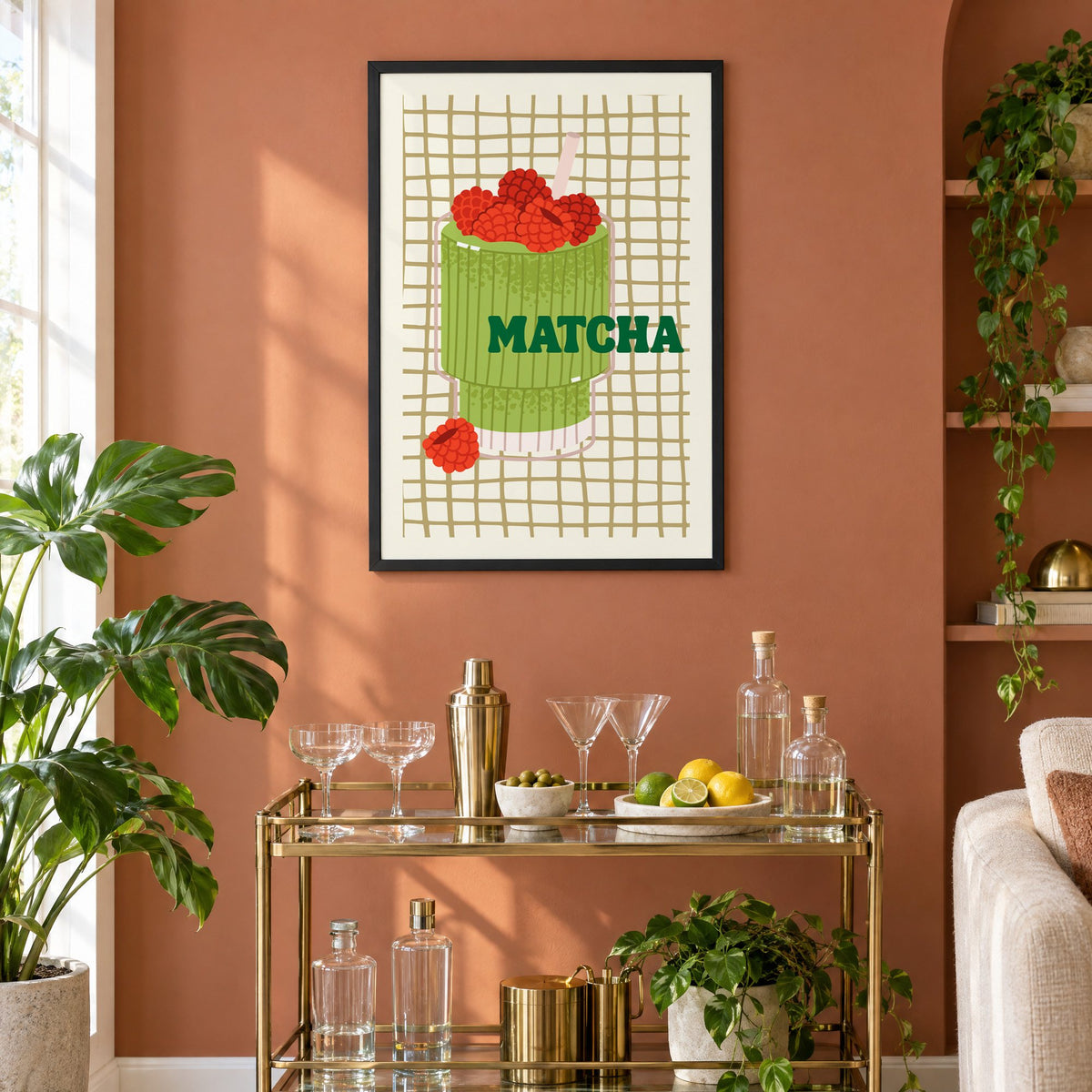 MATCHA raspberry glass on grid print in a black frame on a terracotta wall above a brass bar cart with coupes and citrus