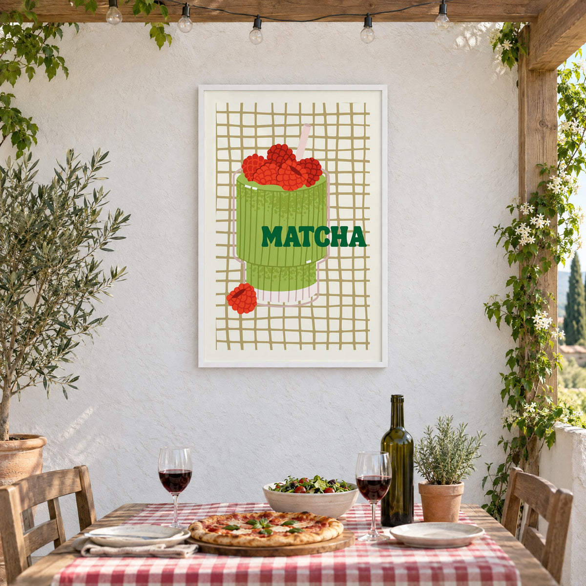 MATCHA raspberry glass on grid print in a white frame on a stucco wall above a checked-cloth table with pizza and red wine