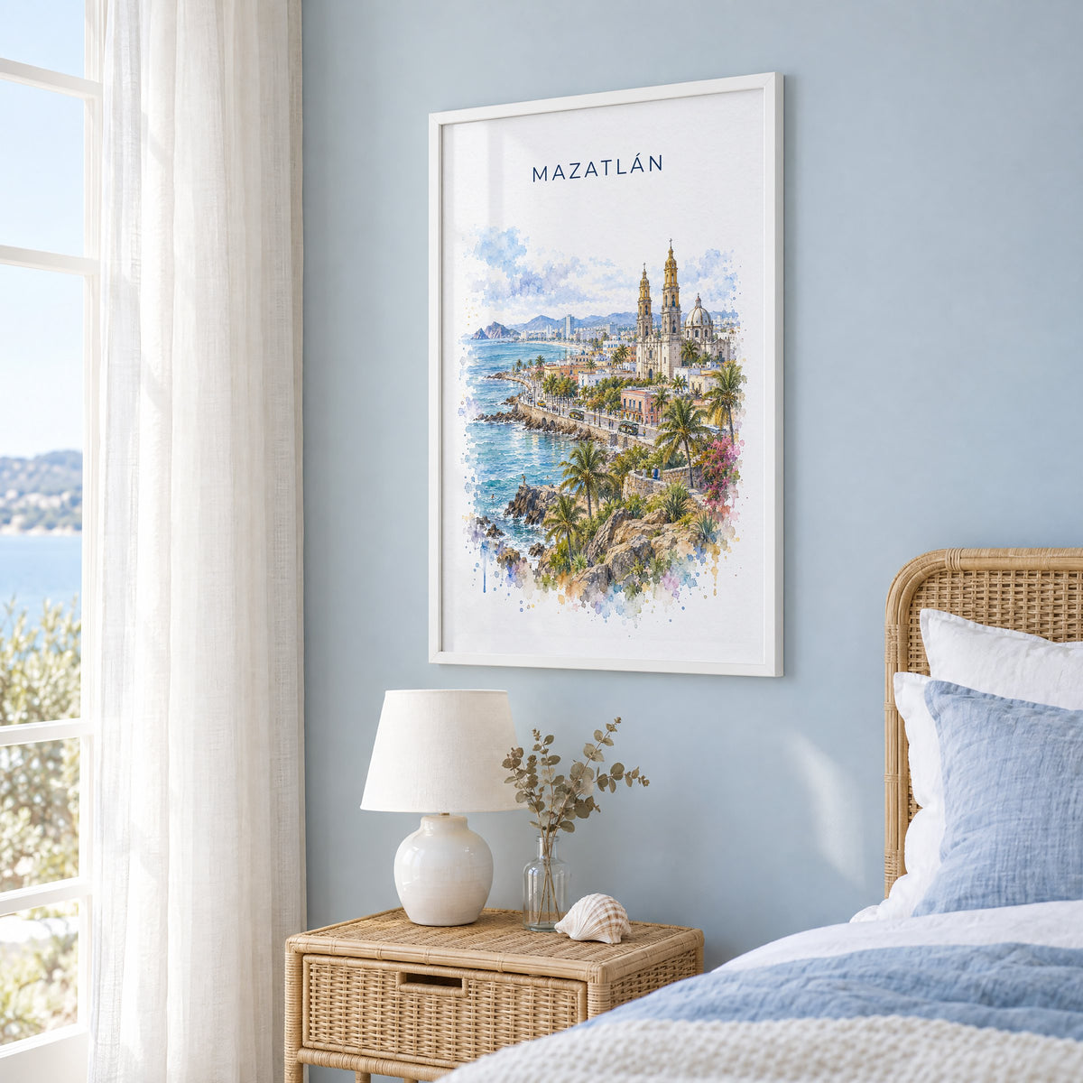 Mazatlan watercolor print in a white frame on a pale blue wall beside a rattan bed in a coastal bedroom
