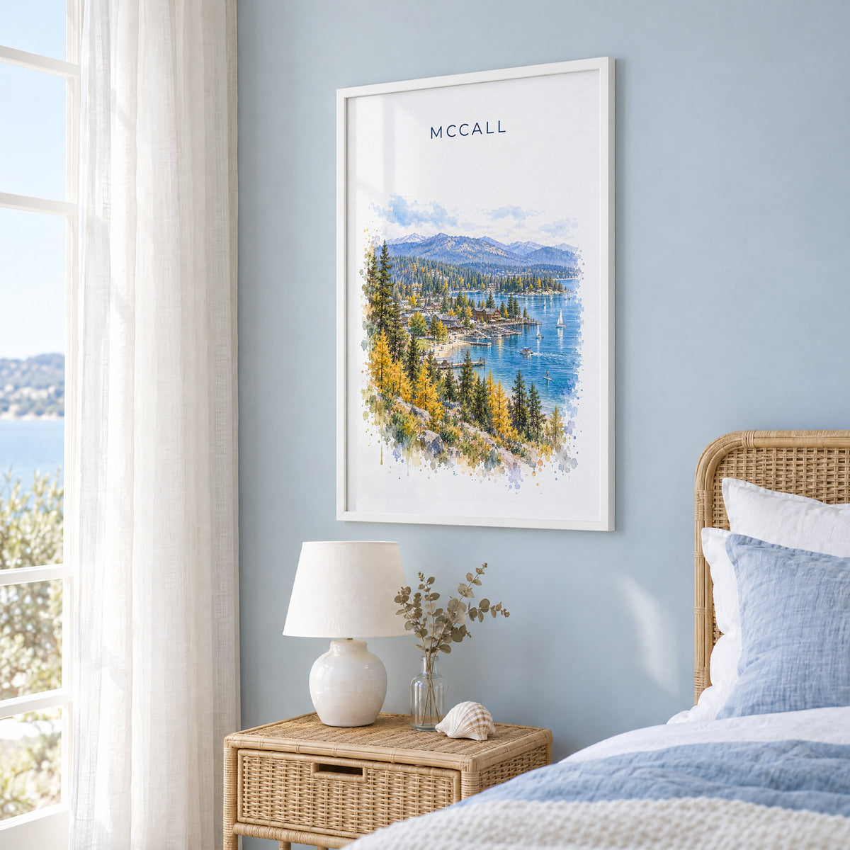 McCall, Idaho watercolor print in a white frame on a pale blue wall beside a rattan bed in a coastal bedroom