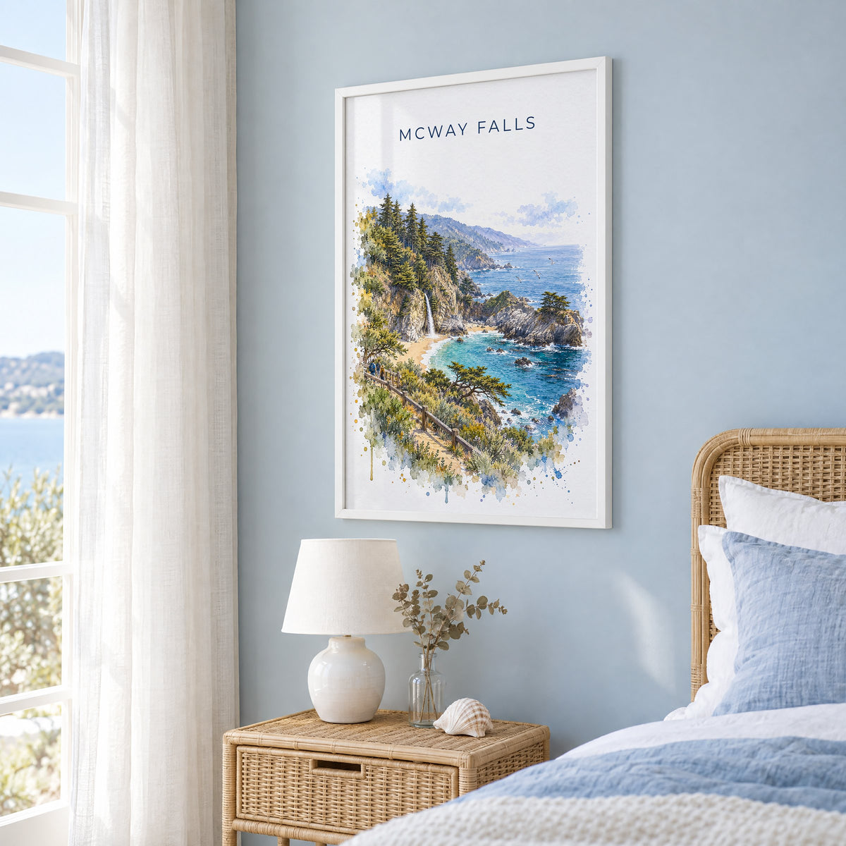 McWay Falls watercolor print in a white frame on a pale blue wall beside a rattan bed in a coastal bedroom