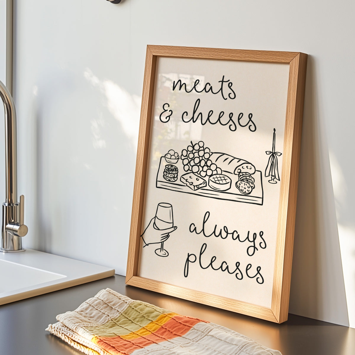 Charcuterie board print in an oak frame by the kitchen sink with a striped tea towel