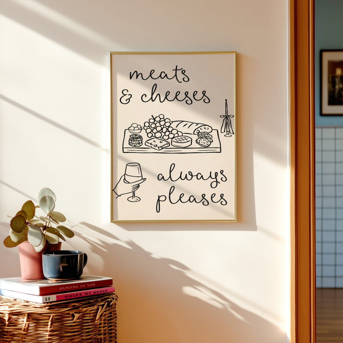 Charcuterie board print in a gold frame above a basket of books and a pilea plant