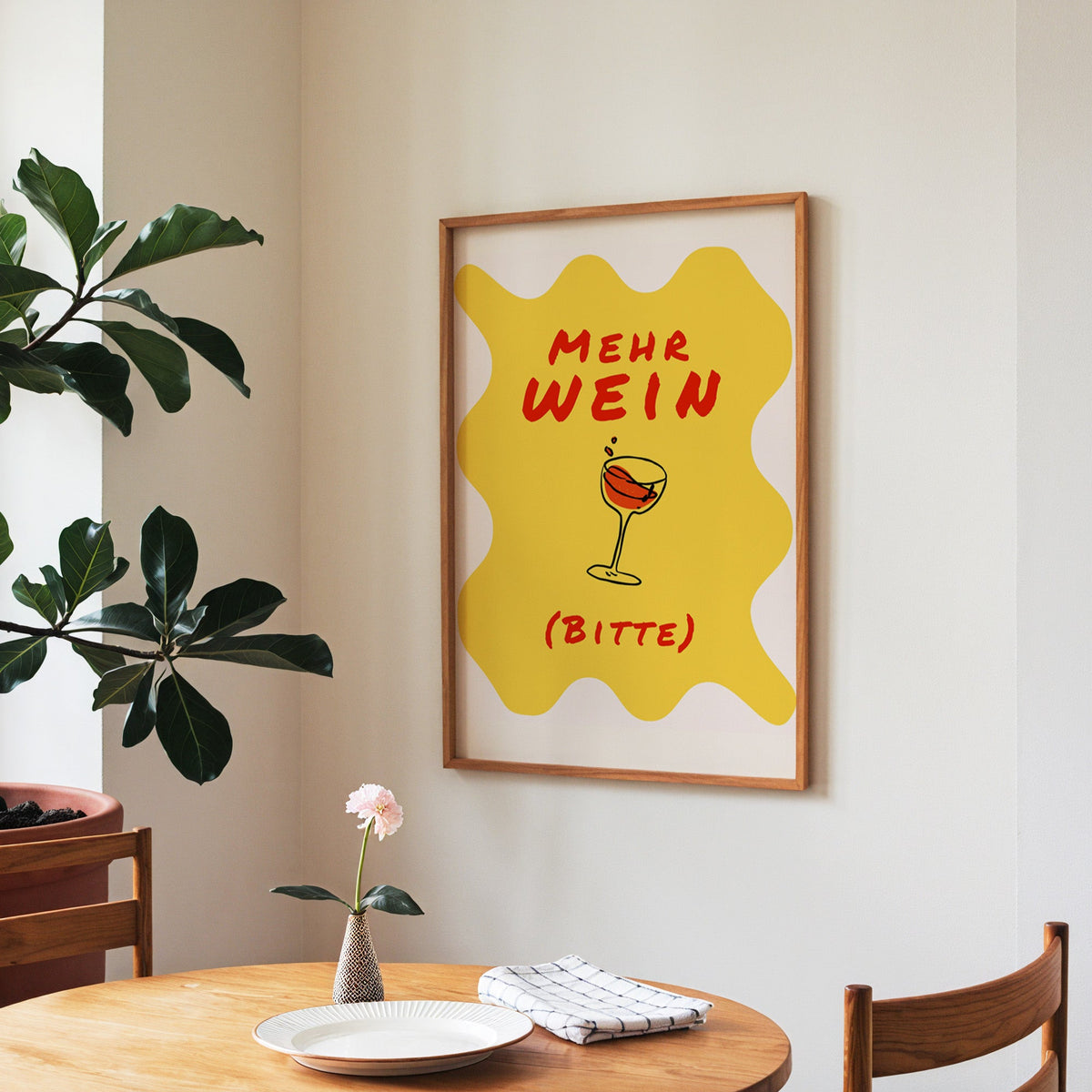 Mehr Wein Bitte print in a walnut frame above a round table beside a fiddle-leaf fig