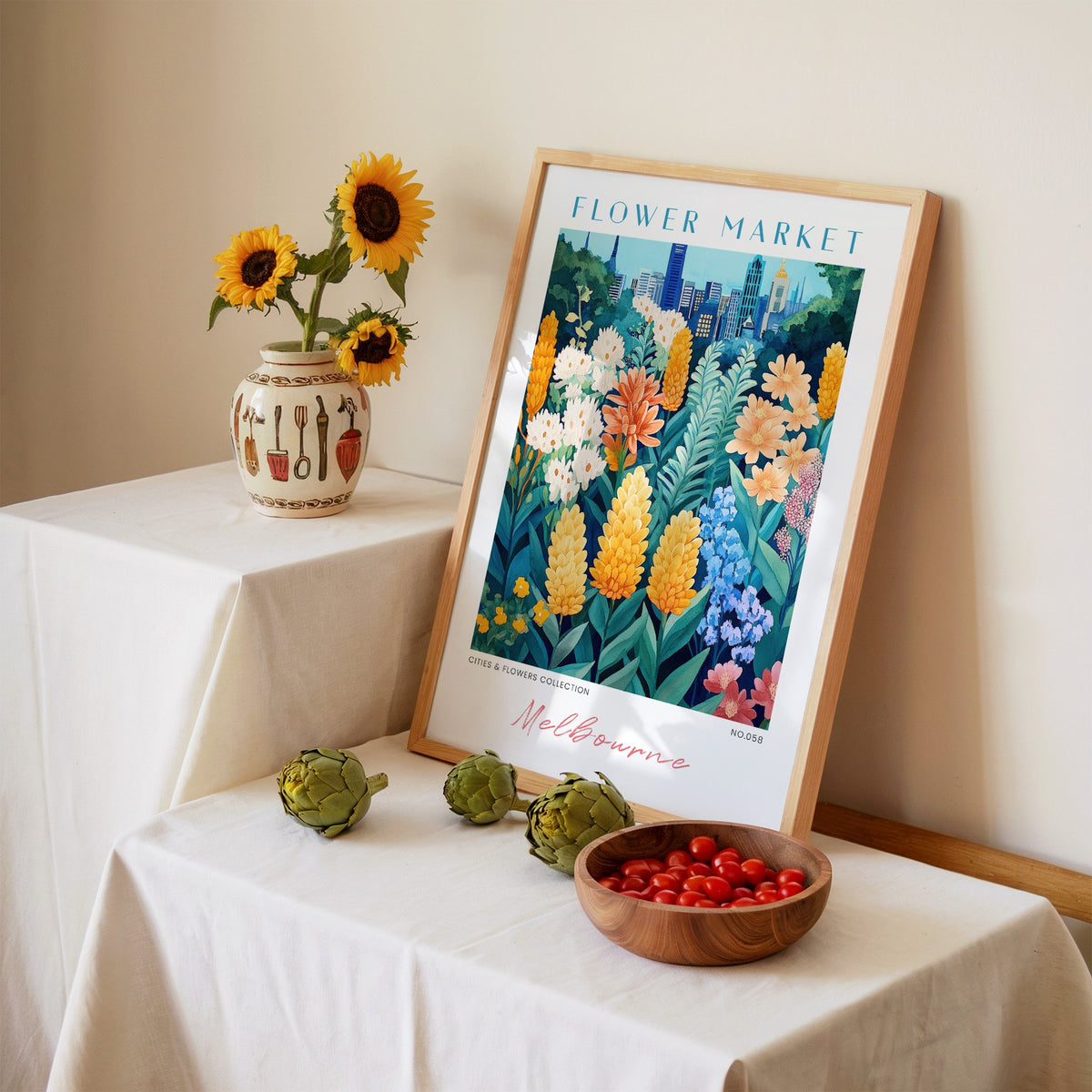 Melbourne flower market print in an oak frame leaning on a linen-draped table beside a vase of sunflowers