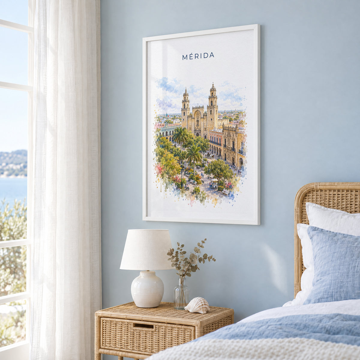 Merida, Mexico watercolor print in a white frame on a pale blue wall beside a rattan bed in a coastal bedroom