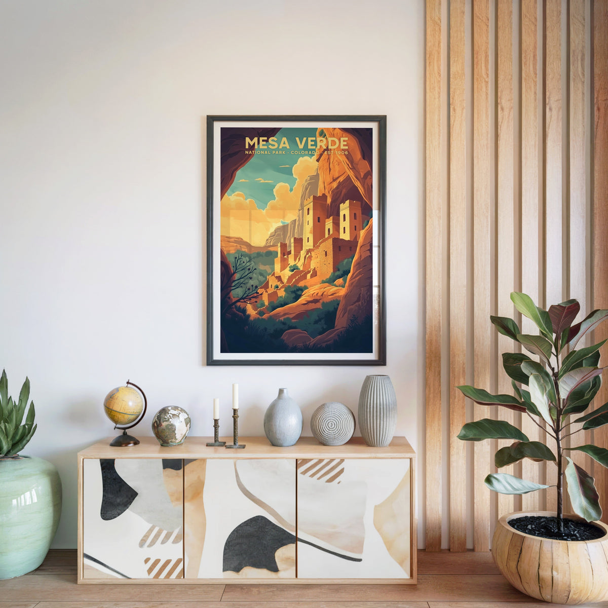 Mesa Verde National Park print in a black frame above a light wood sideboard with a globe and ceramic vases
