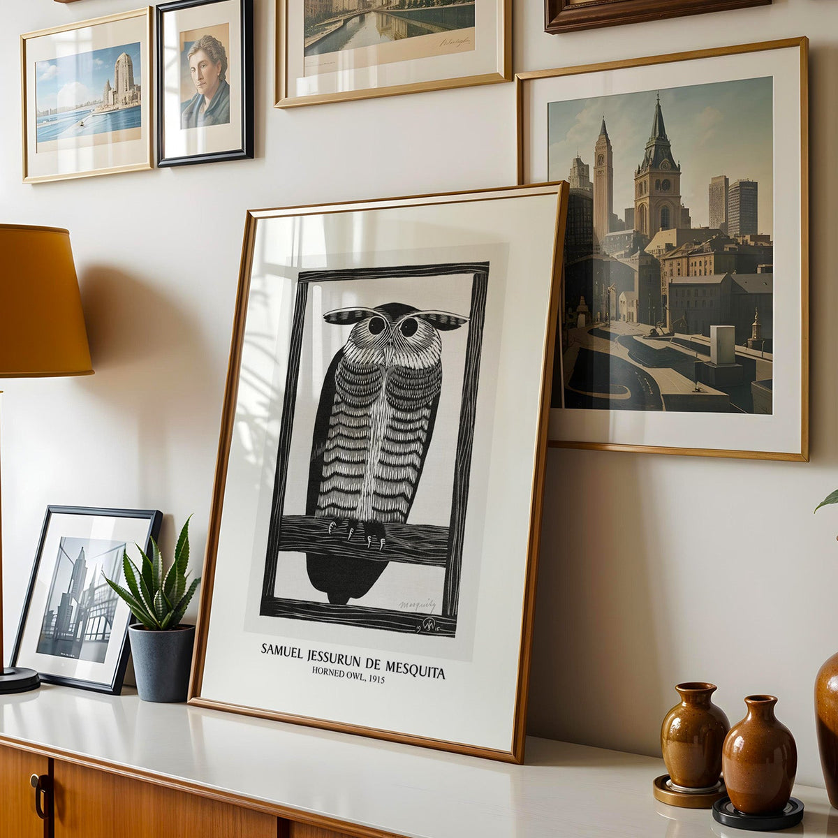 Owl print shown in a gold frame leaning on a sideboard in a gallery wall