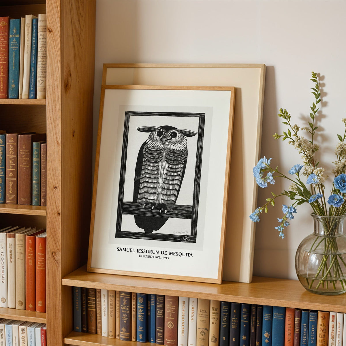 Horned owl woodcut in an oak frame leaning on a bookshelf beside blue flowers
