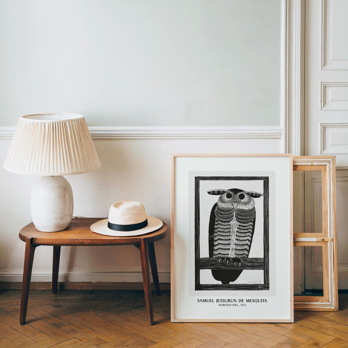 Woodcut owl poster in a light wood frame leaning by a bench and panama hat