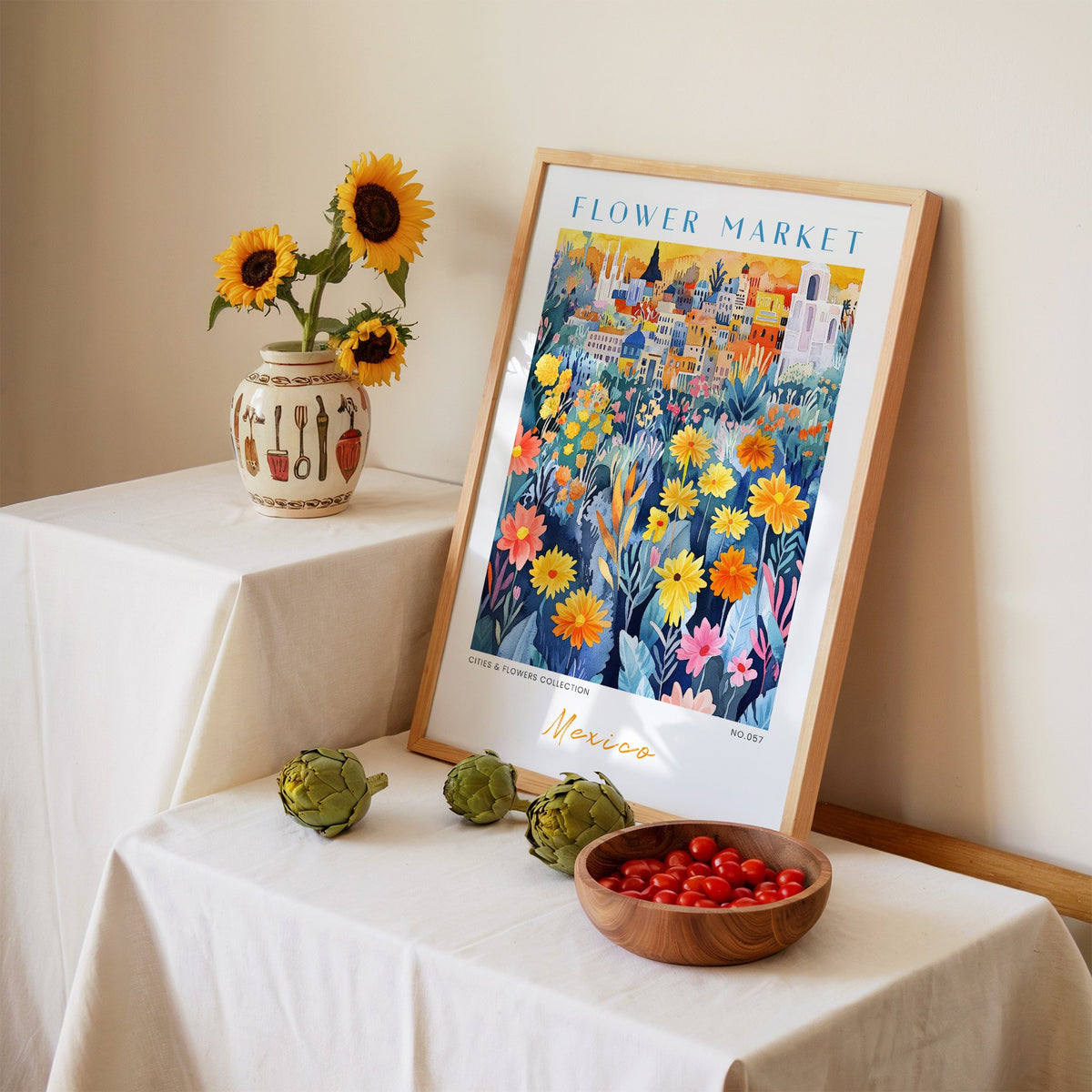 Mexico flower market print in an oak frame leaning on a linen-draped table beside a vase of sunflowers