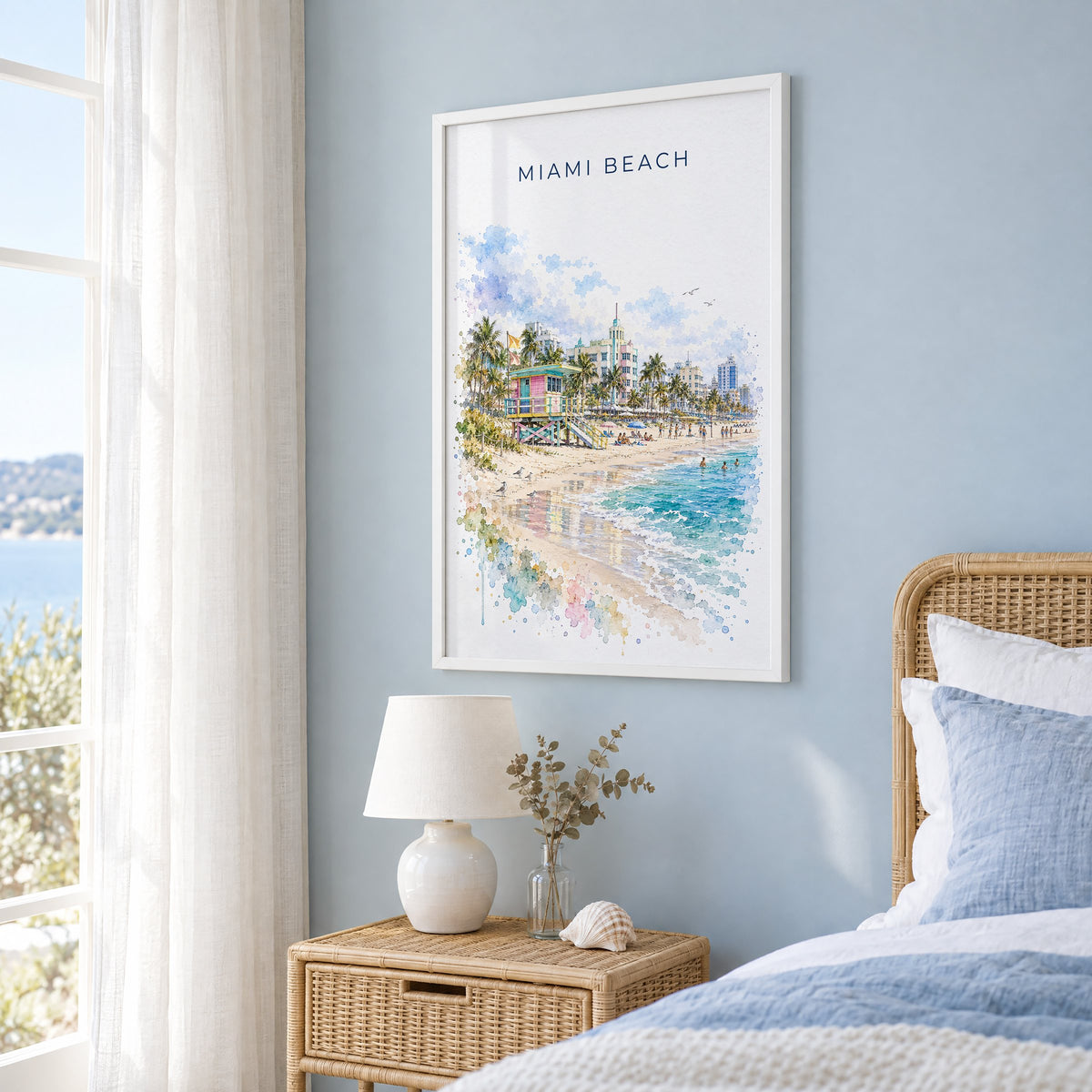 Miami Beach watercolor print in a white frame on a pale blue wall beside a rattan bed in a coastal bedroom