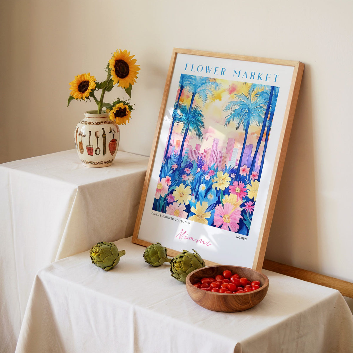 Miami flower market print in an oak frame leaning on a linen-draped table beside a vase of sunflowers