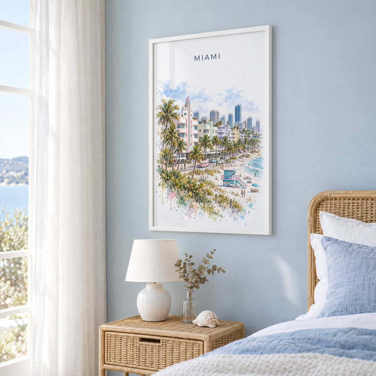 Miami watercolor print in a white frame on a pale blue wall beside a rattan bed in a coastal bedroom