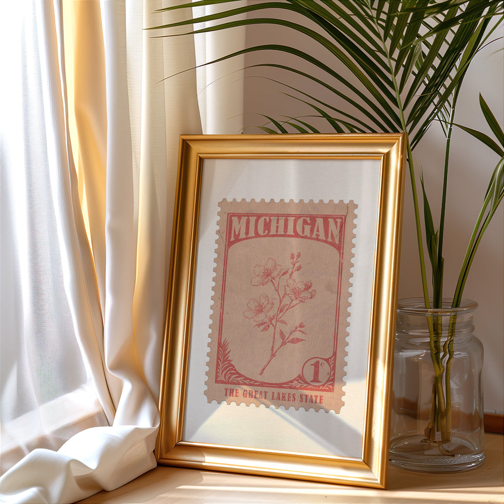 Michigan stamp print in a gold frame leaning by a cream curtain with a palm in a glass jar