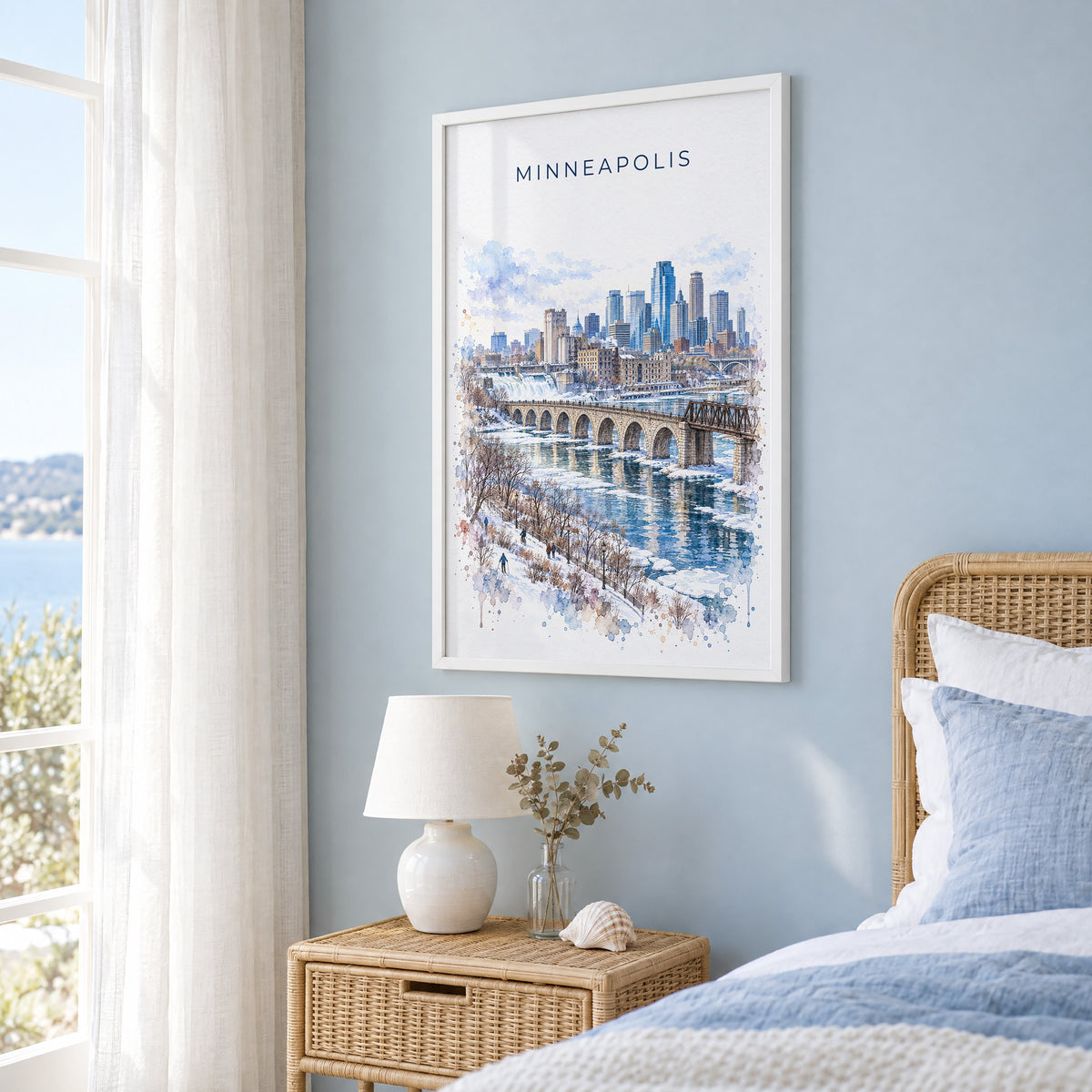 Minneapolis watercolor print in a white frame on a pale blue wall beside a rattan bed in a coastal bedroom