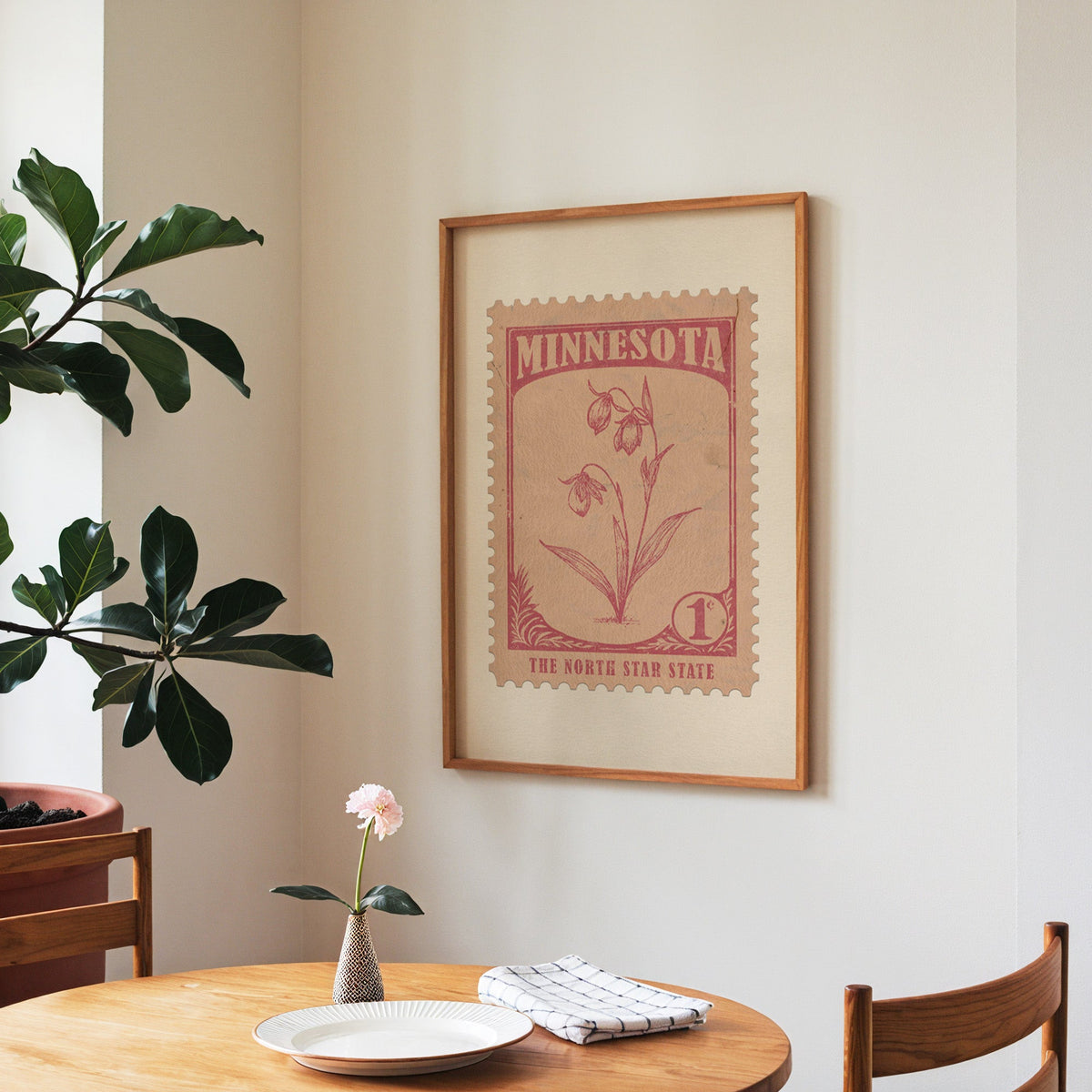 Minnesota state flower print framed above a round wooden table with a single bloom in a vase and books