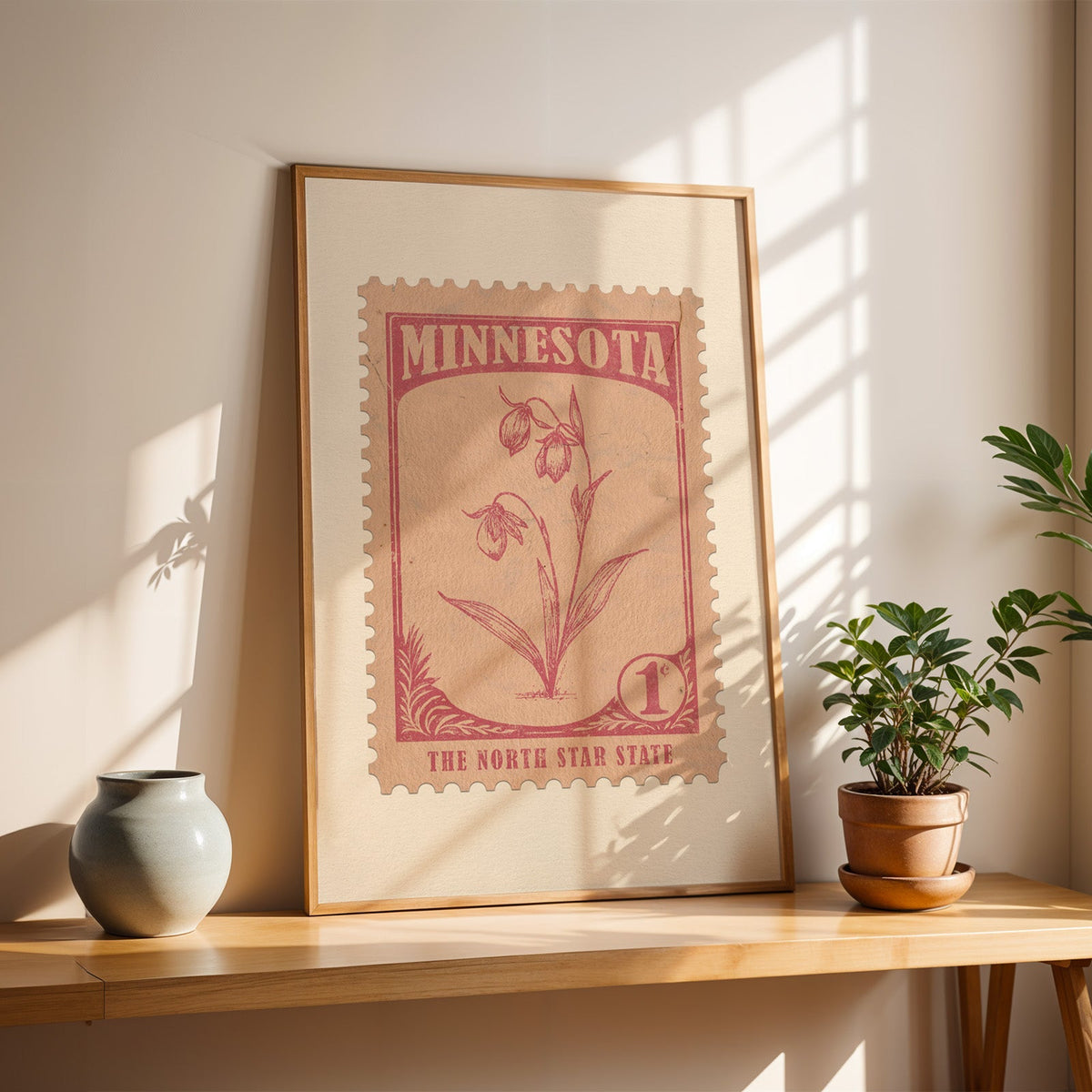 Minnesota Lady's Slipper stamp print in a light oak frame leaning on a wooden table beside a stoneware vase