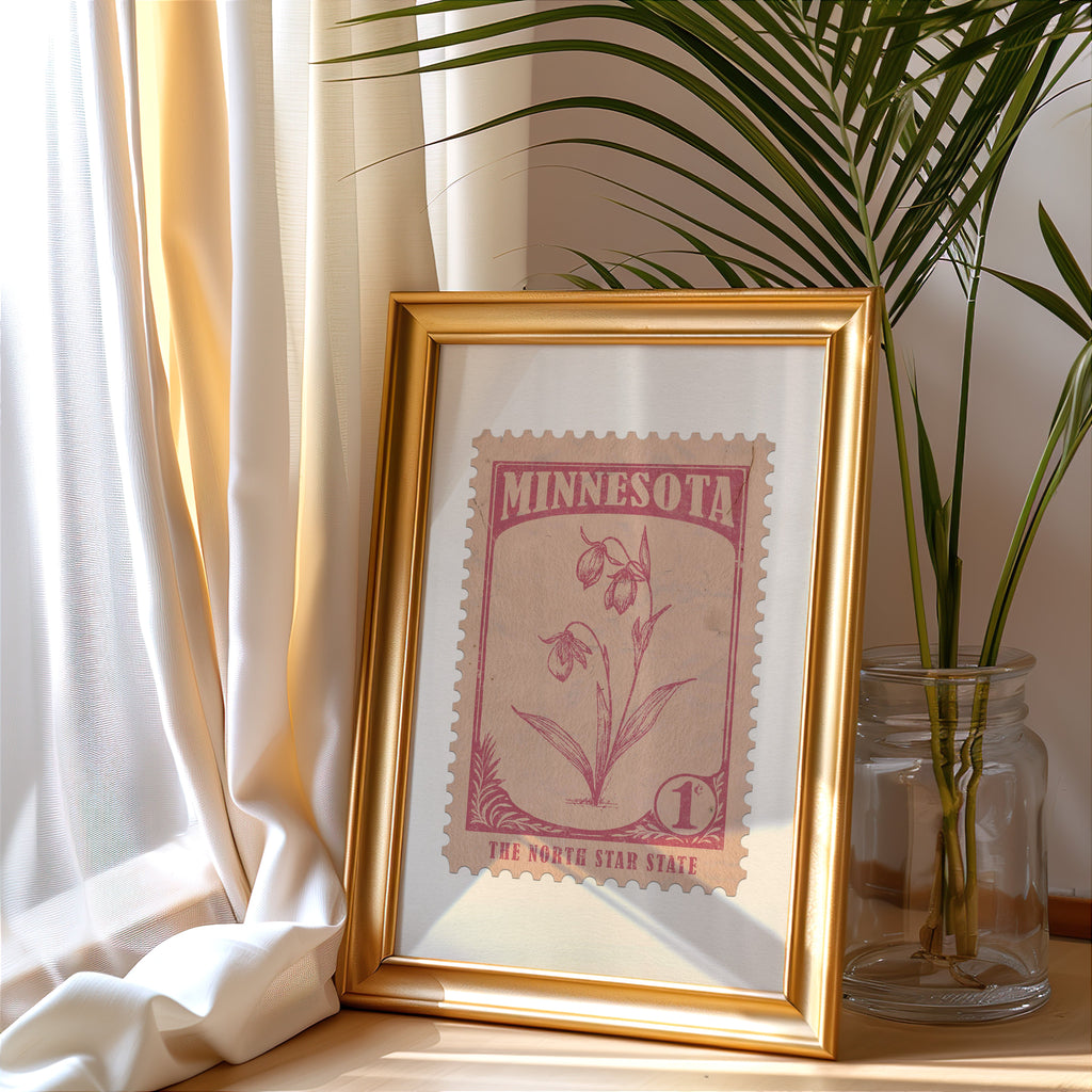 Minnesota stamp print in a gold frame leaning by a cream curtain with a palm in a glass jar