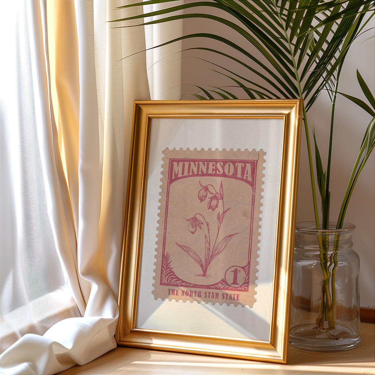 Minnesota stamp print in a gold frame leaning by a cream curtain with a palm in a glass jar